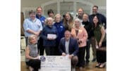 A group of men and women cluster around a large replica of a check