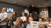 A packed meeting room with Cobb County residents, many holding protest signs.