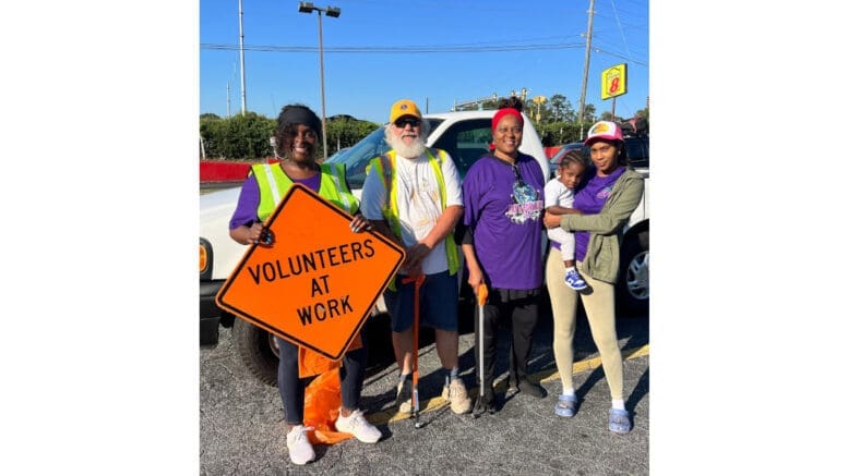 A group shot of the volunteers at the Cityview Drive litter cleanup, one holding a "volunteers at work" sign