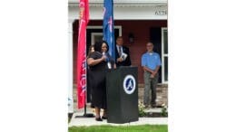 Quintasha Swanson speaking at lectern in front of Habitat for Humanity house