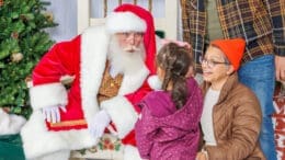 Santa with a little girl while an elf looks on