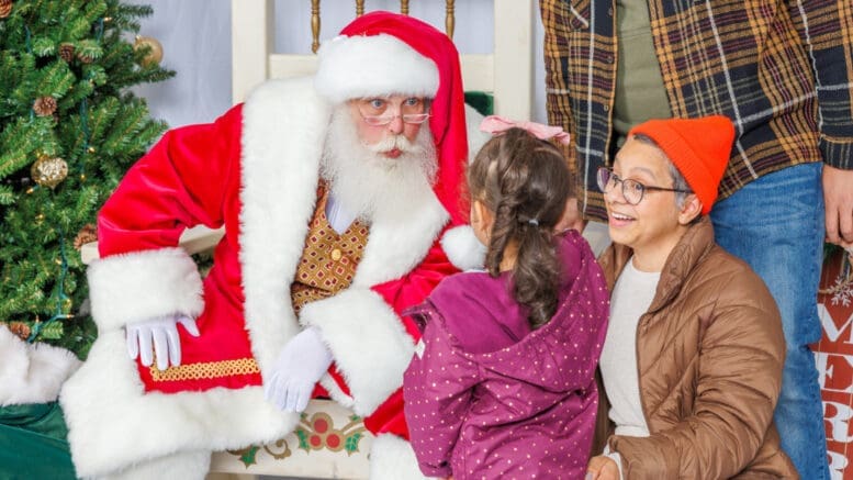 Santa with a little girl while an elf looks on