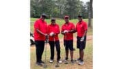 Four men in red shirts with golf clubs pose for a group photo