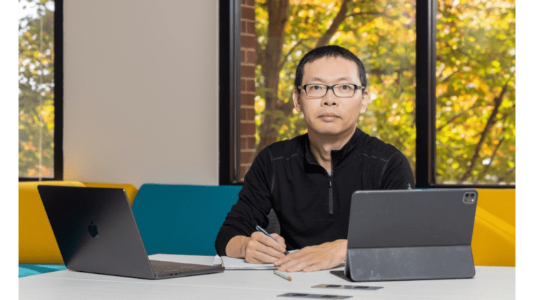 Kennesaw State University researcher Liang Zhao sits a a desk, surrounded by papers and a laptop computer