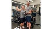 Woman and man standing by exercise equipment in a gym, smiling, woman raising dumbell in one hand