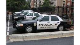 A row of Kennesaw Police Department cruisers with multifamily buildings past a black metal fence