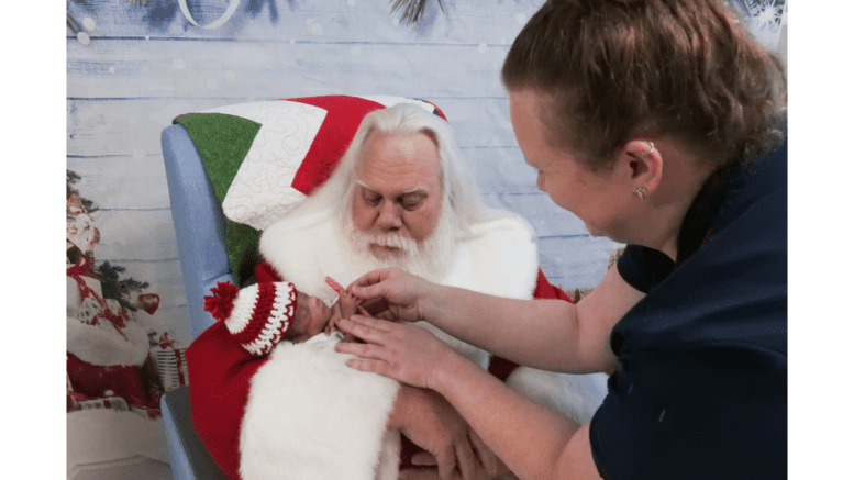 Santa holds a tiny infant while a woman extends a candy cane toward the baby