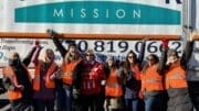 A group of Sweetwater Mission volunteers and staff cheering in front of one of the organization's food distribution trucks