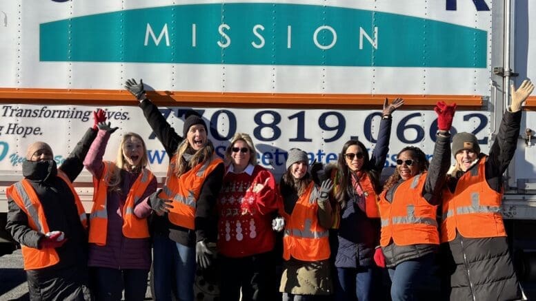 A group of Sweetwater Mission volunteers and staff cheering in front of one of the organization's food distribution trucks