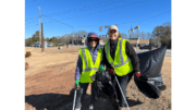 Two smiling Keep Smyrna Beautiful volunteers wearing yellow safety vests, with litter pickup poles and plastic bags