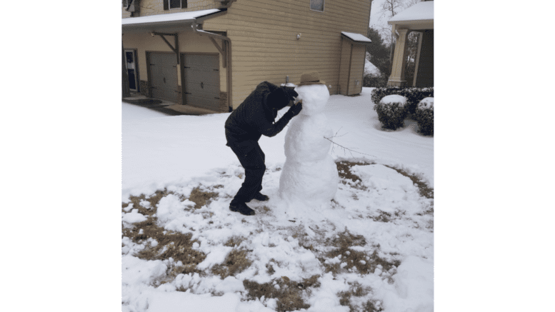 A man puts the orange nose on a snowman