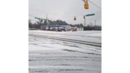 Snowy roadway and Chevron station at the intersection of Veterans Memorial Highway and Oakdale Road/Discovery Blvd. A highway road sign hangs over the intersection