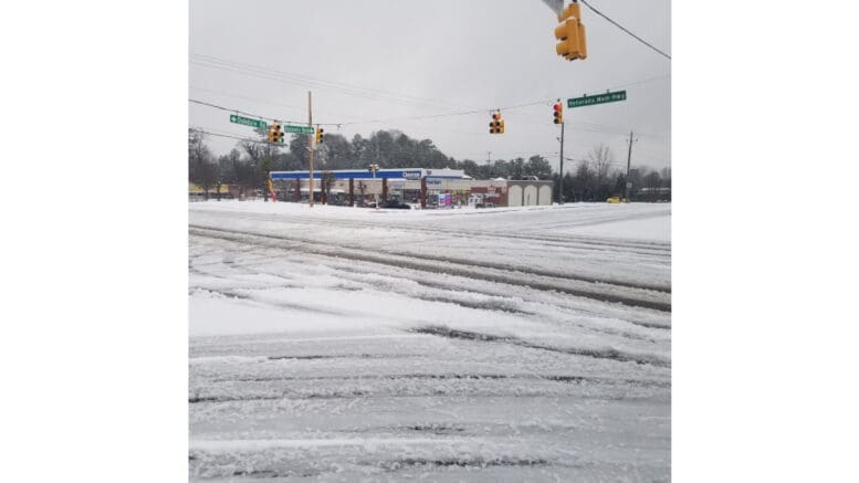 Snowy roadway and Chevron station at the intersection of Veterans Memorial Highway and Oakdale Road/Discovery Blvd. A highway road sign hangs over the intersection