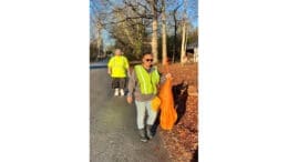 Woman in yellow safety vest carrying a bag of litter collected on the James Road adopt-a-mile cleanup. A man, also in a safety vest, follows her