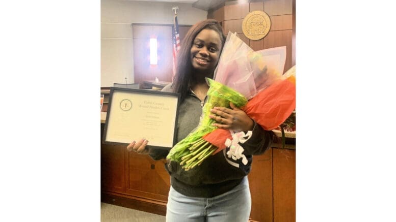 A smiling woman holds flowers and a certificate from Cobb Mental Health Court