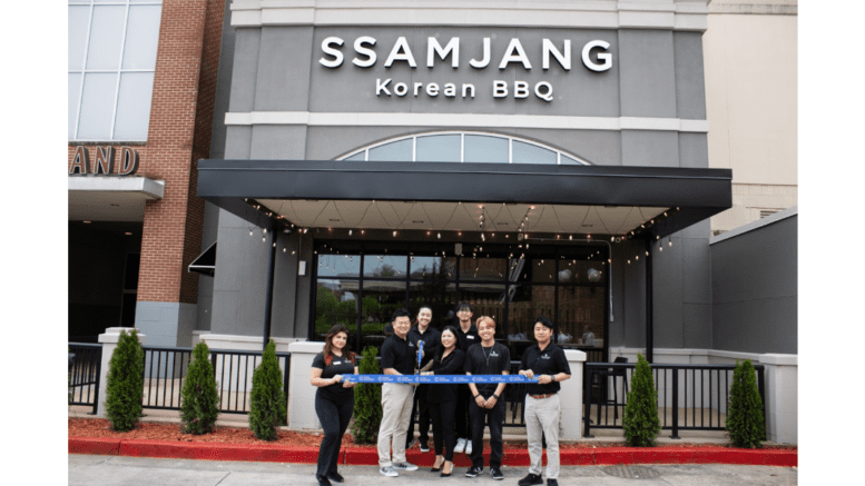 A group photo at a ribbon-cutting ceremony at SSamJang Korean BBQ, with the signage for the restaurant in the background