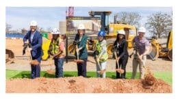 A row of people with hardhats shoveling dirt at a groundbreaking ceremony