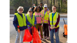 Group photo of volunteers at a Vinings Cove cleanup on Buckner Road. The volunteers are wearing yellow safety vests and two are holding red trash bags.