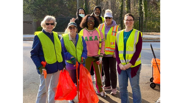 Group photo of volunteers at a Vinings Cove cleanup on Buckner Road. The volunteers are wearing yellow safety vests and two are holding red trash bags.