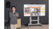 Jian Zhang standing with microphone in front of presentation board
