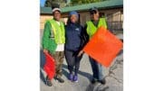 Three women wearing safety vests and holding traffic direction flags; in a group photo, smiling