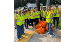 Group photo of the Atlanta Latino Lions Club wearing yellow safety vests, with orange full bags of litter from their cleanup of Windy Hill Road