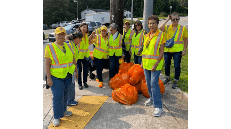 Group photo of the Atlanta Latino Lions Club wearing yellow safety vests, with orange full bags of litter from their cleanup of Windy Hill Road