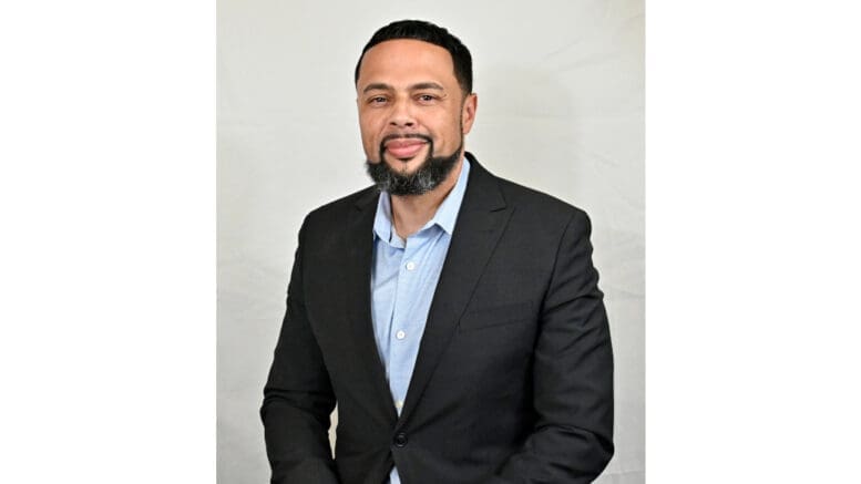 Michael McNeely upper body shot. McNeely is wearing a dark suit jacket and blue open-collared shirt