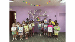 A group of little girls holding up books in front of a tree sculpture