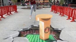 a 3-D chalk art rendering that looks like a jagged break in the pavement hovering above a soccer field