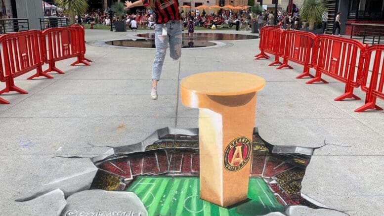 a 3-D chalk art rendering that looks like a jagged break in the pavement hovering above a soccer field