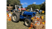 A child sits on a blue tractor surrounded by harvest-themed items