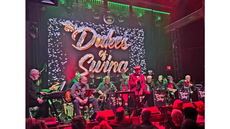 The band Dukes of Swing sit, with instruments, onstage