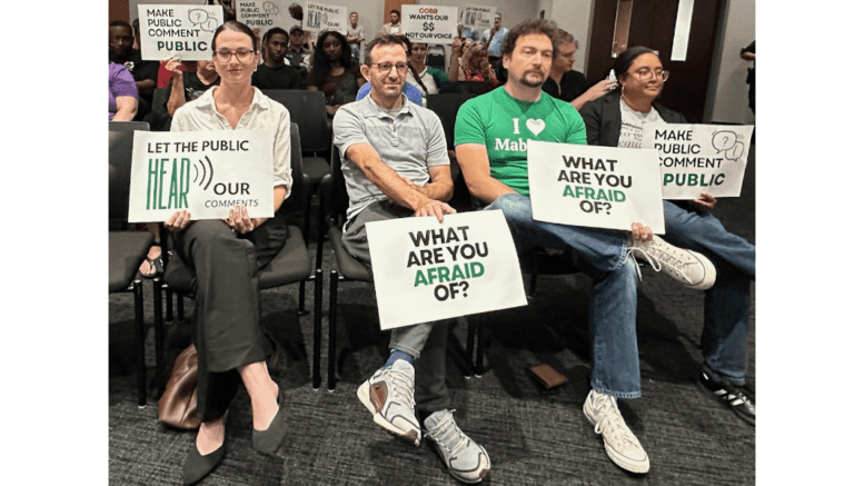 People seated with signs protesting the Cobb schools censoring of public comments
