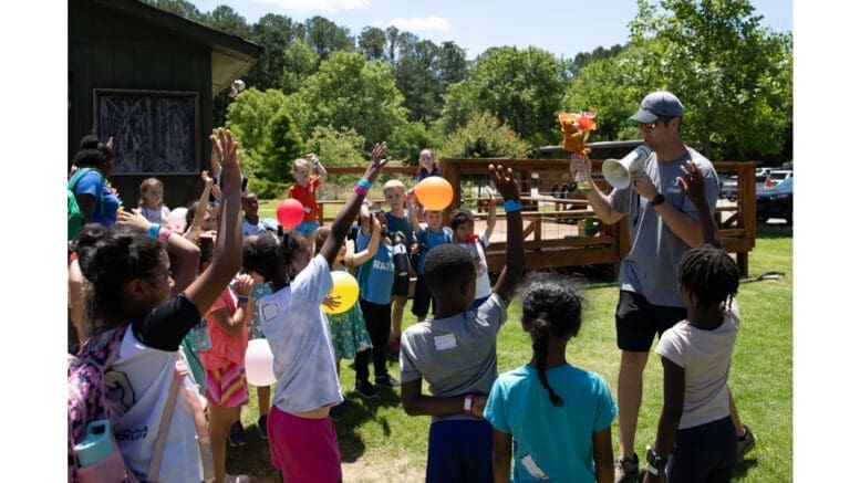 Kids at YMCA summer camp gathered around adult camp counselor