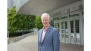 Tom Rowland in coat and dress shirt without tie stands in front of the Cobb Energy Performing Arts Centre where he has been appointed managing director